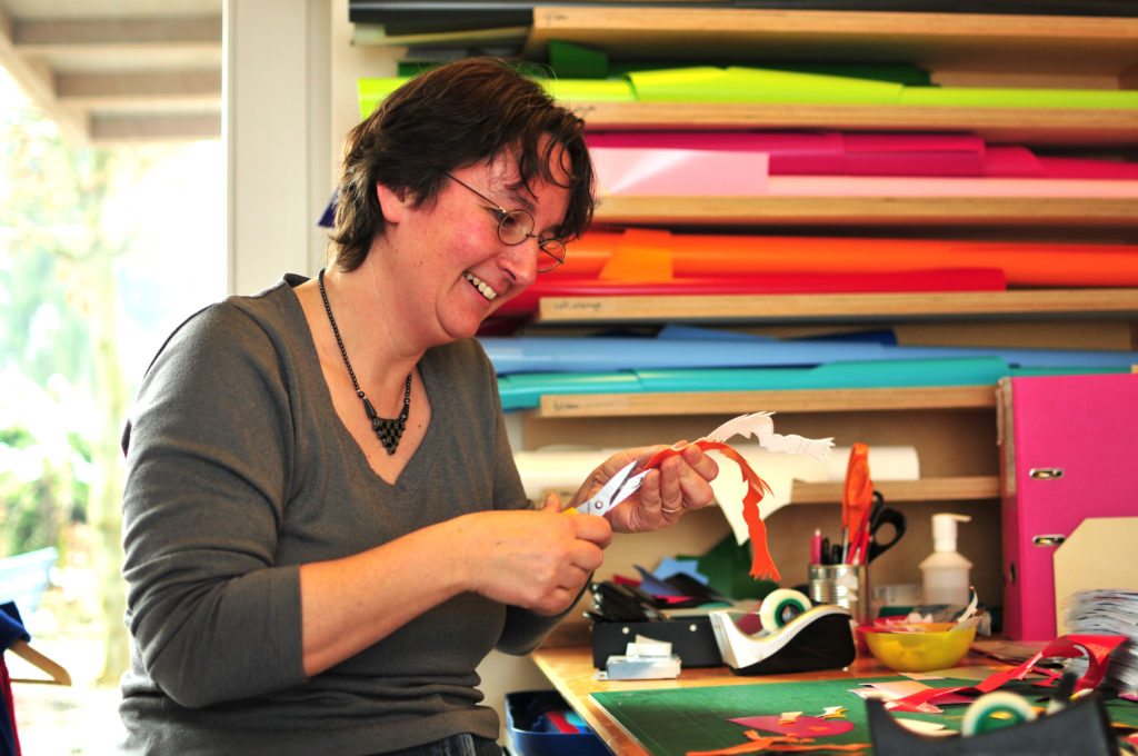 cwirbelwind-Mitarbeiterin Käthi schneidet ein Motiv aus Blachenstoff für ein Chindsgitäschli zu.